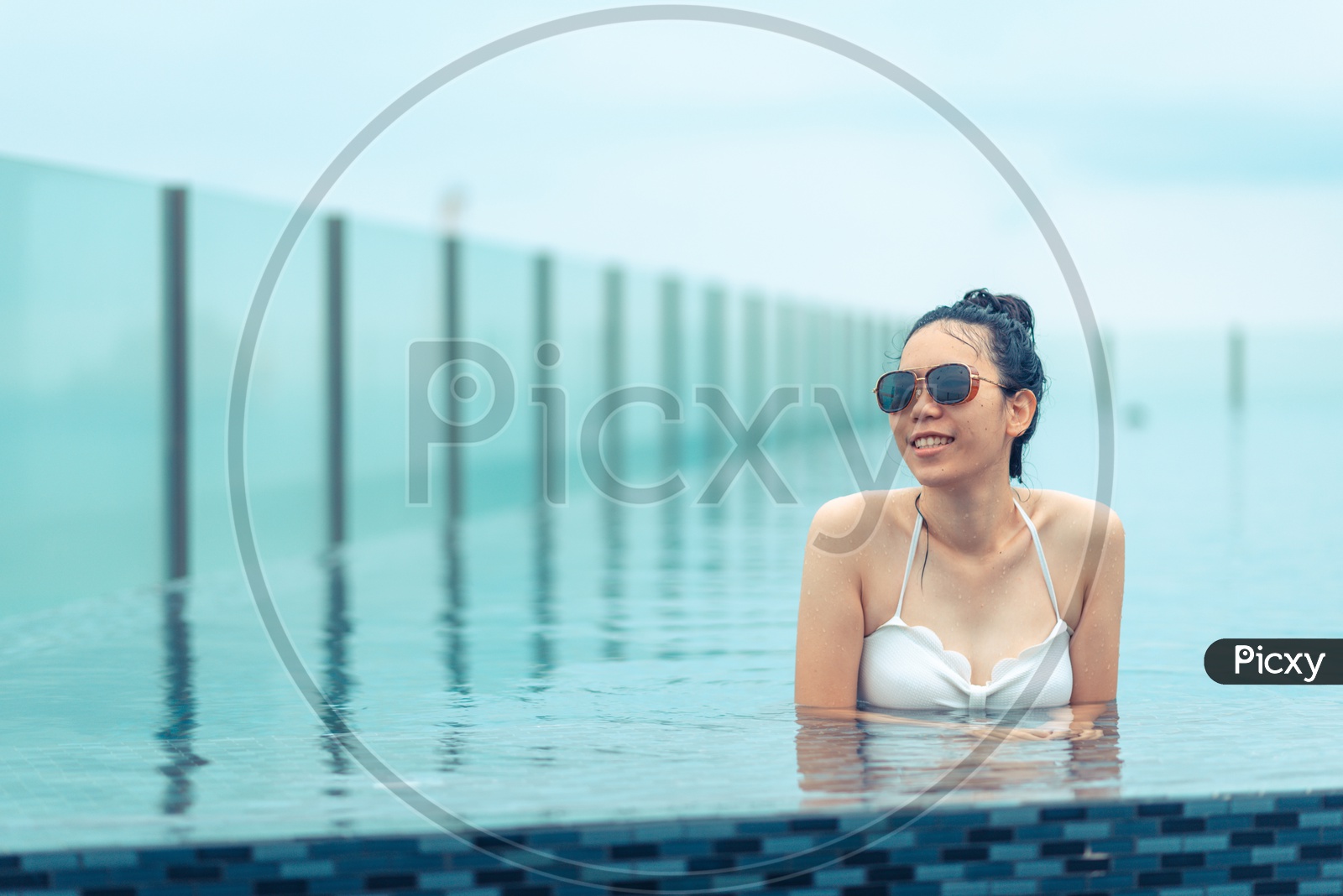 Asian girl wearing swimsuit and sunglasses in Swimming pool on roof top