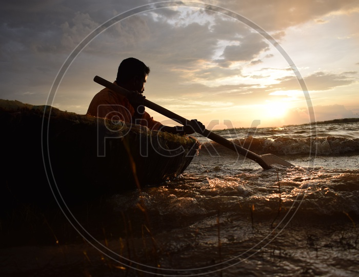 Fisherman rowing is oars in water, sea looking at sunset