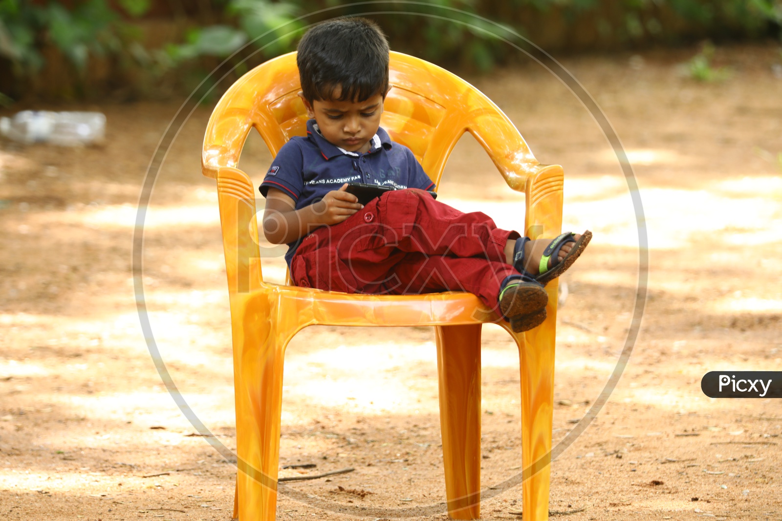 Indian little boy sitting on a chair playing games on the smartphone