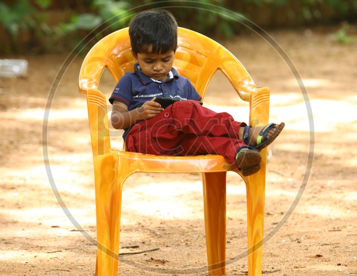 Indian little boy sitting on a chair playing games on the smartphone