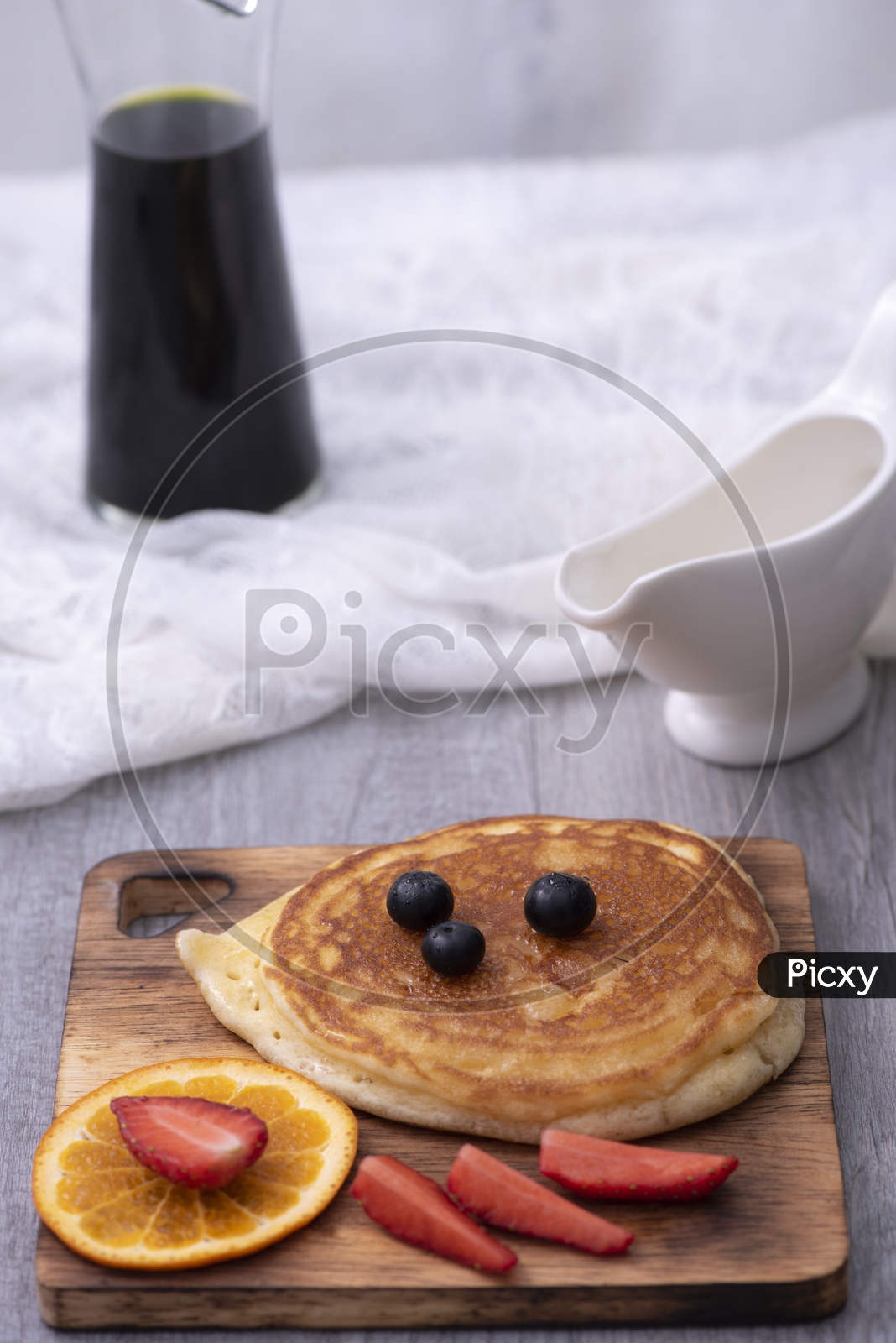 Homemade pancakes with berries and honey on a pink plate over white wooden surface