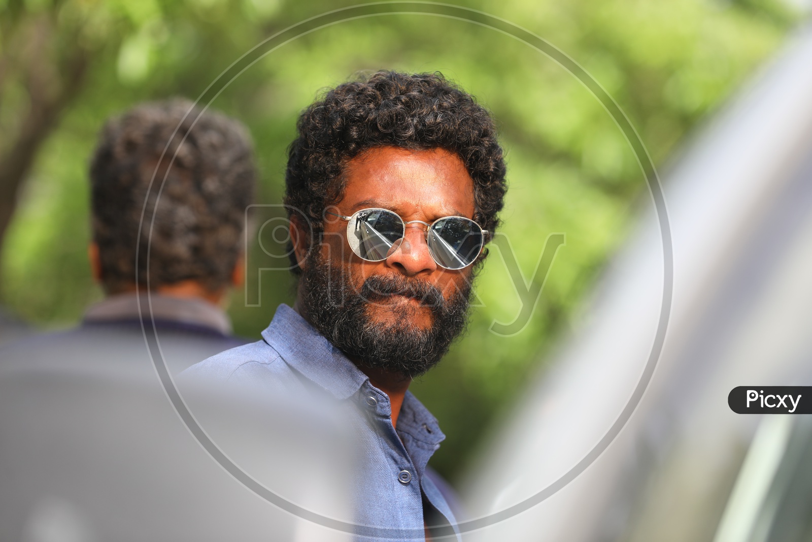 An Indian man with facial hair and curly hair wearing Sunglasses