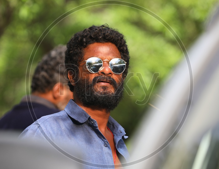An Indian man with facial hair and curly hair wearing Sunglasses