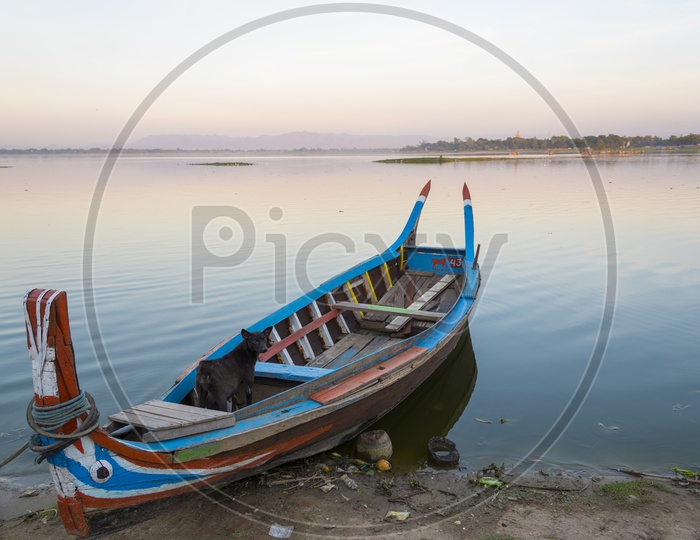 A Wooden boat tied to the shore along Ubein Bridge during sunrise in Mandalay, Myanmar
