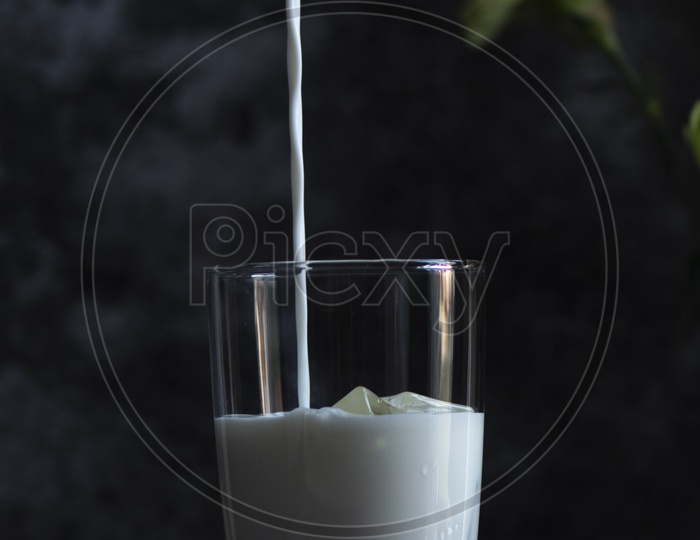 Pouring  fresh milk into a glass with ice.