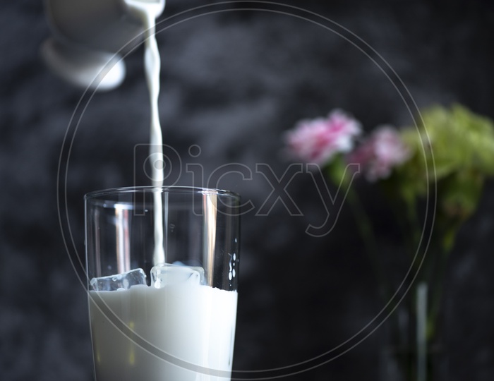 Pouring  fresh milk into a glass with ice.