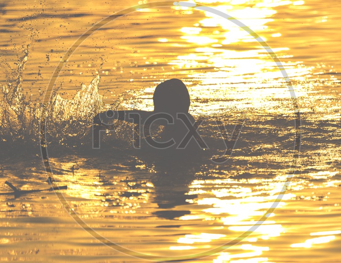 Silhouette Of a Boy Child Swimming In a Lake Over Bright Sunset Light