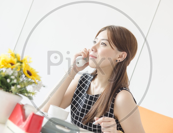 Asian  young business woman on phone taking notes in office