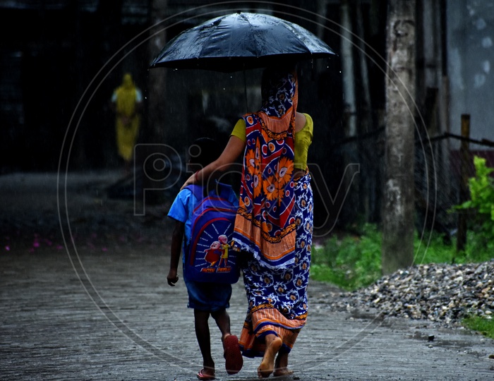 In a wet/ rainy morning a mother took her son to the school holding the umbrella over their heads .