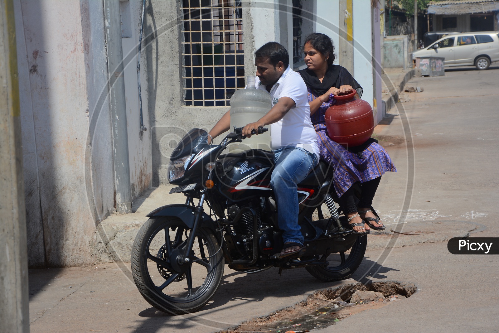 A Couple Carrying Drinking Water Filled Vessels In a Bike