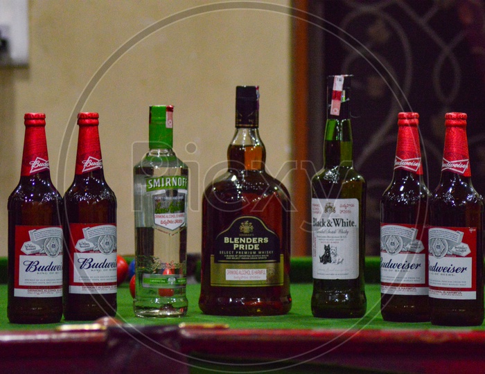 A display of various alcoholic beverages like Smirnoff, Blenders Pride, Budweiser and Black & White on a Pool Table