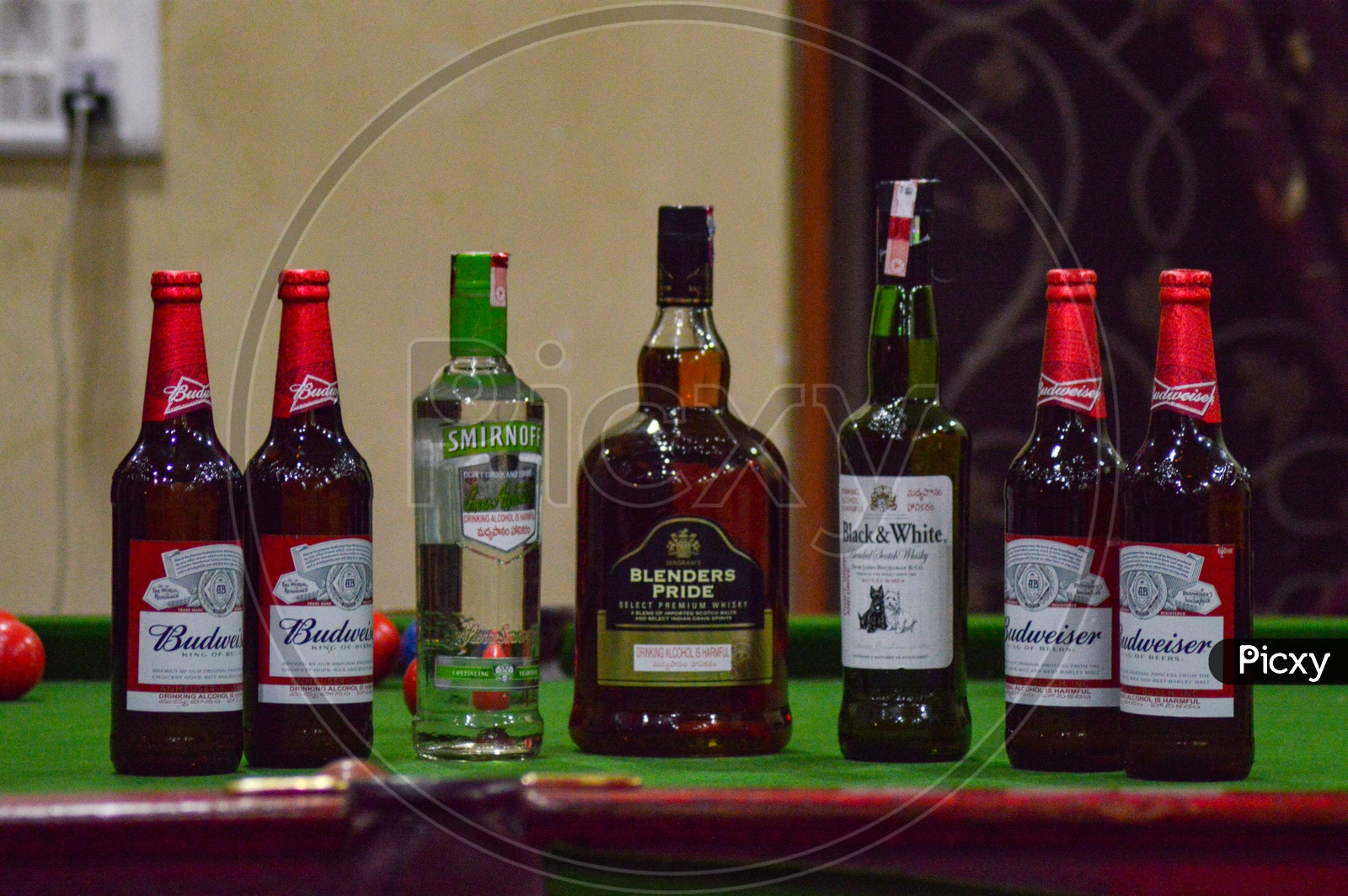 A display of various alcoholic beverages like Smirnoff, Blenders Pride, Budweiser and Black & White on a Pool Table