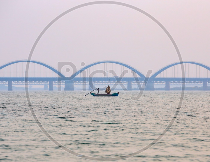 Fisherman Riding Boat On Godavari River With Arch Bridge In Background