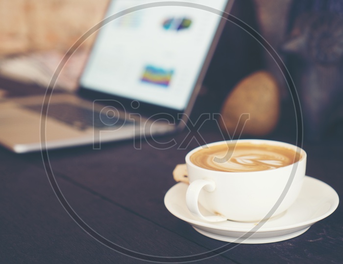 Coffee Latte Art With Coffee Cup in a Cafe Over Laptop Bokeh Background , Working in Cafe Concept