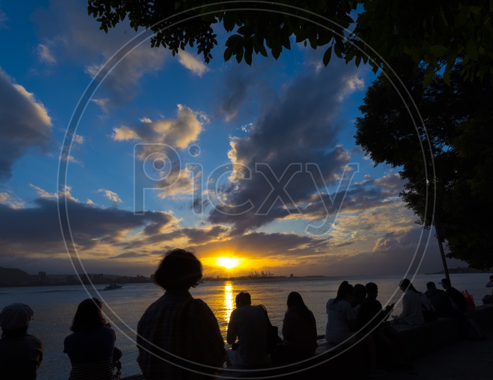 Silhouette Of People Sitting And Enjoying The Sunset Over A River