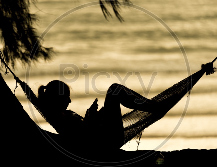 Silhouette Of A Young Girl Using Smartphone At Beach With Golden Sun Light