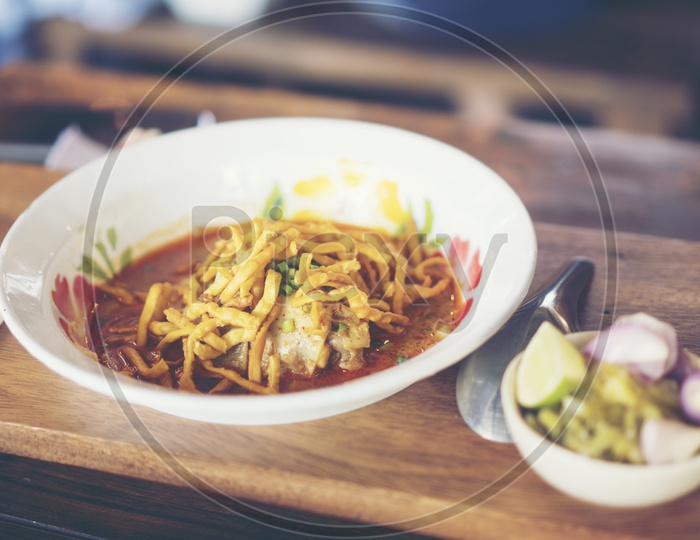 Khao Soi or Khao Soy Soup With Chicken And Crisp Noodles Topped over it Served in a Restaurant Table Background