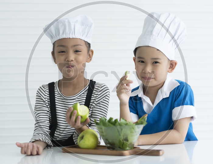 A boy and a girl are eating green apples as little chefs -  cooking concept