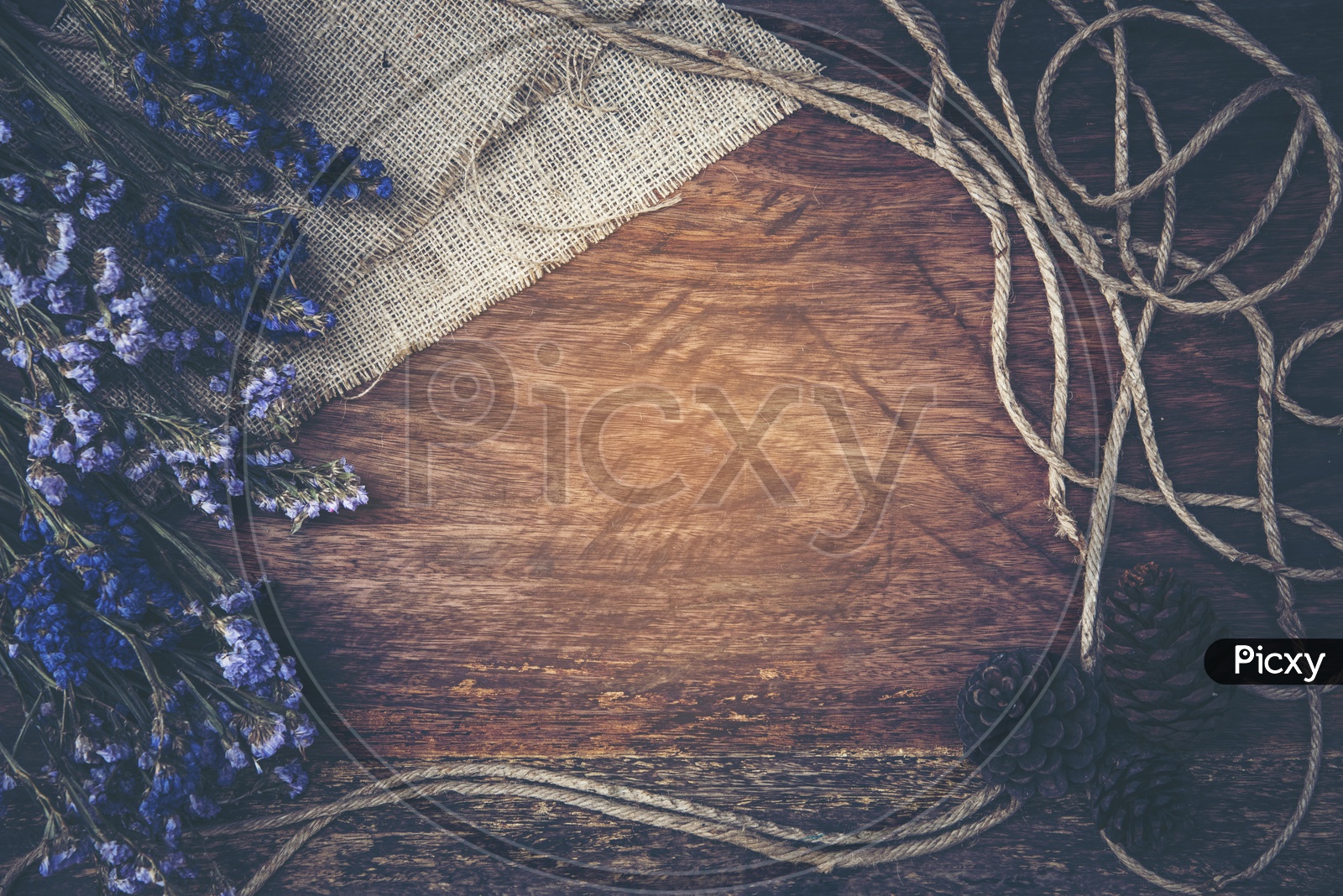 Dry purple flowers and jute thread frame on wood background
