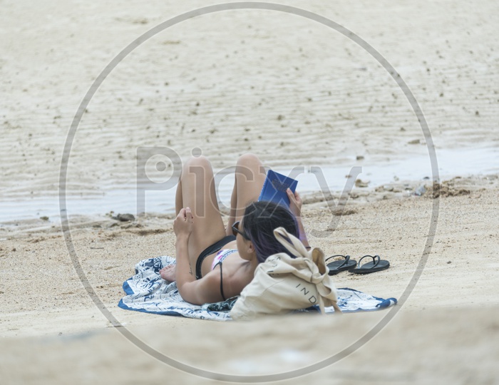 Young  Girl Reading Book In a Beach by Lying in Sand At Phuket