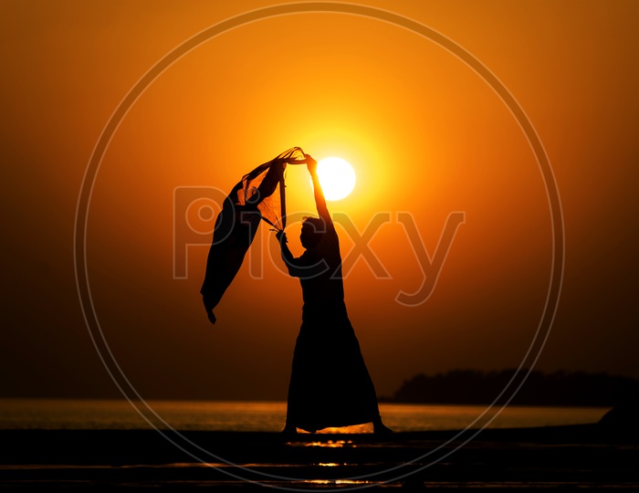 Silhouette of man On a Lake Bank With Scarf In Hands Over a Golden Sky In Background