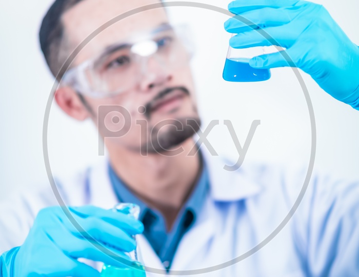 Male Asian Scientist with Hand Gloves Analyzing Chemical Samples in Glass Bottle Apparatus
