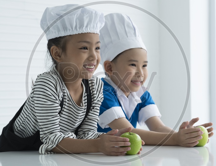 A boy and a girl are playing with green apples as little chefs -  cooking concept