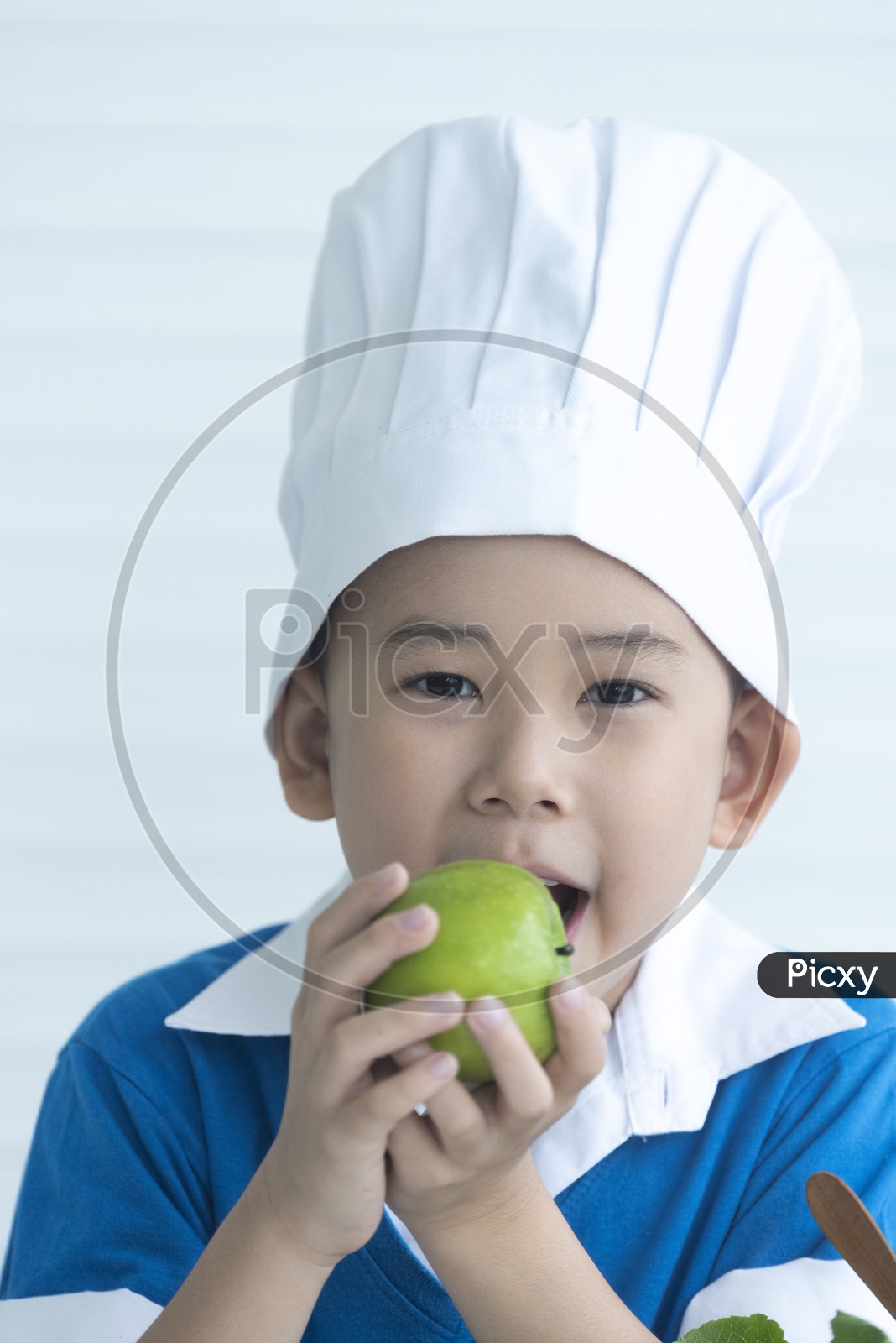 Close up of boy as a chef smiling eating green apple - cooking concept