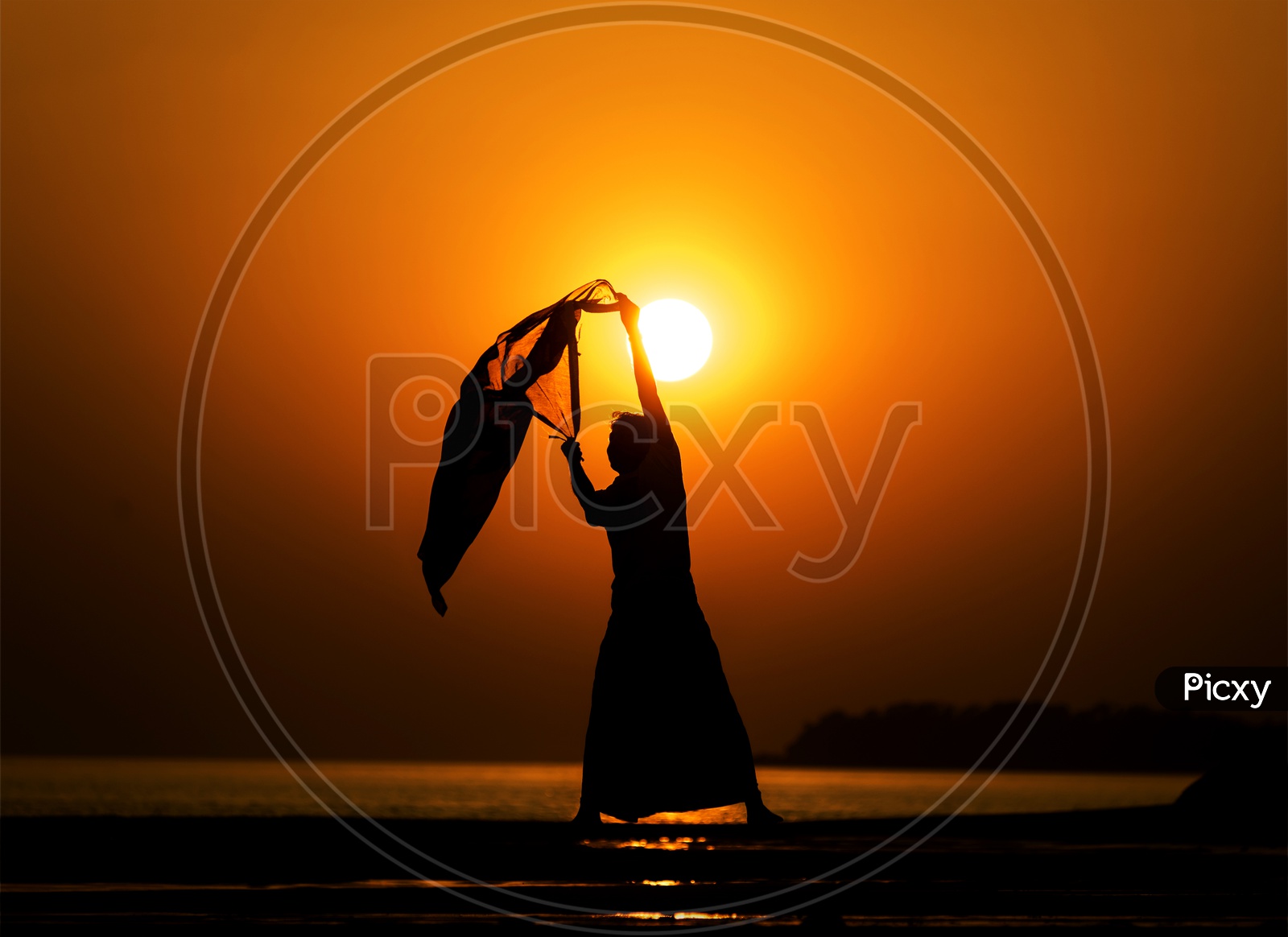Silhouette of man On a Lake Bank With Scarf In Hands Over a Golden Sky In Background