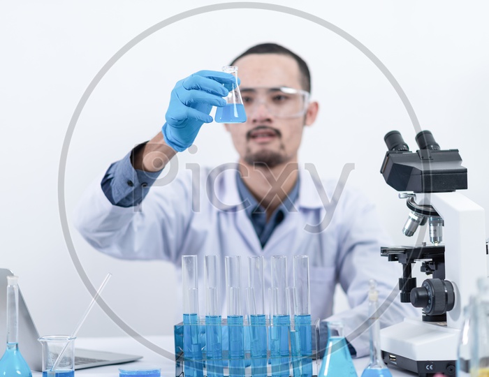 Male Researcher in the laboratory Analyzing Test Tube with Chemicals with Microscope and Test Tubes in Foreground
