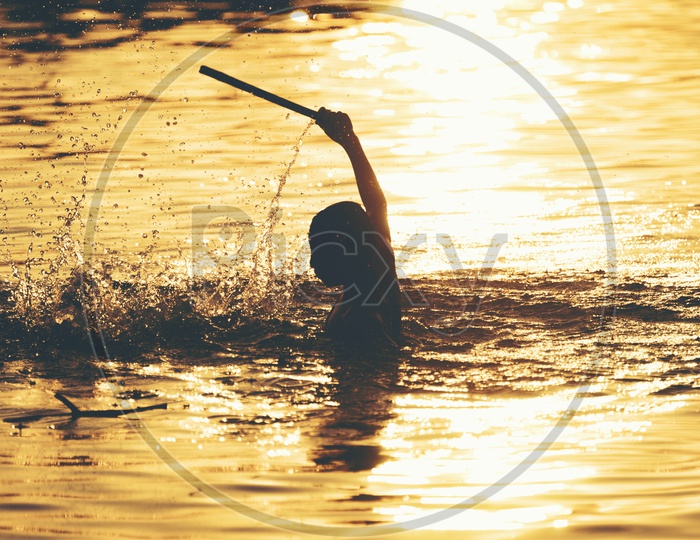 Silhouette of Boy Swimming In  Lake  With Sunset Golden Light