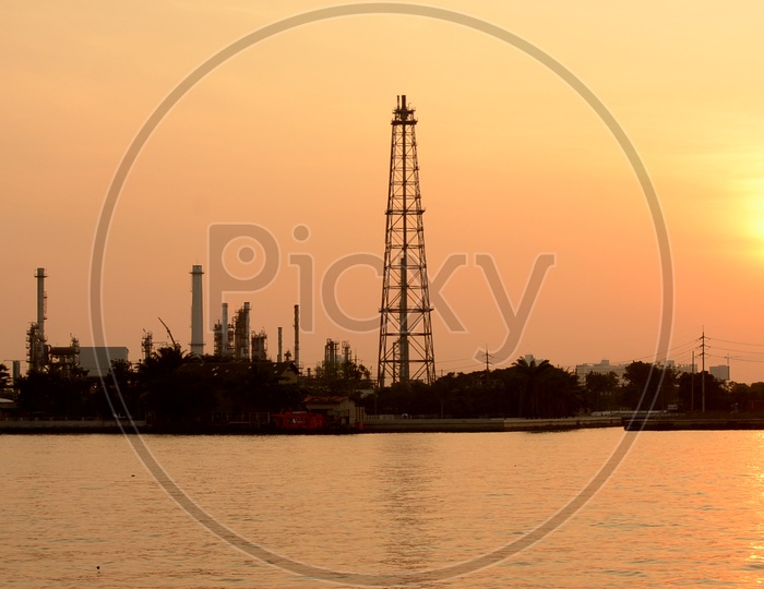 Silhouette of Oil Refinery Plat Besides Lake  With Exhaust Pipes And Towers of Industry over a Sunset Sky in Background