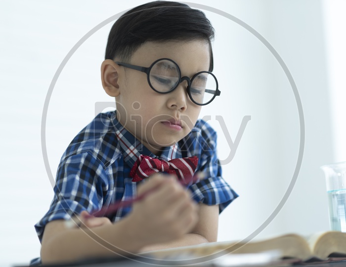 A school boy with specs writing in a book with a pencil
