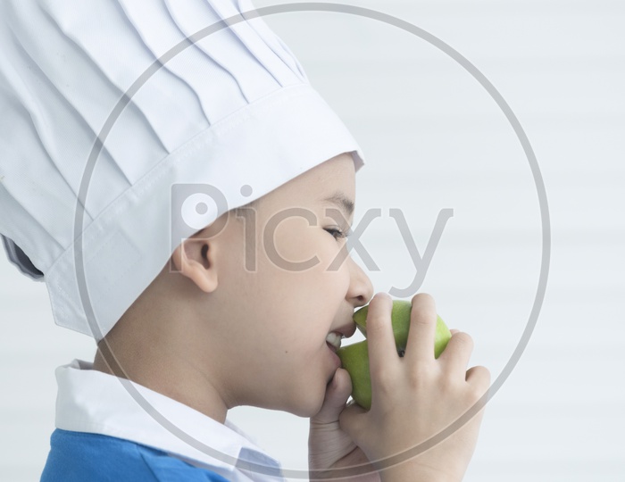 Close-up of boy eating green apple as a chef smiling - cooking concept