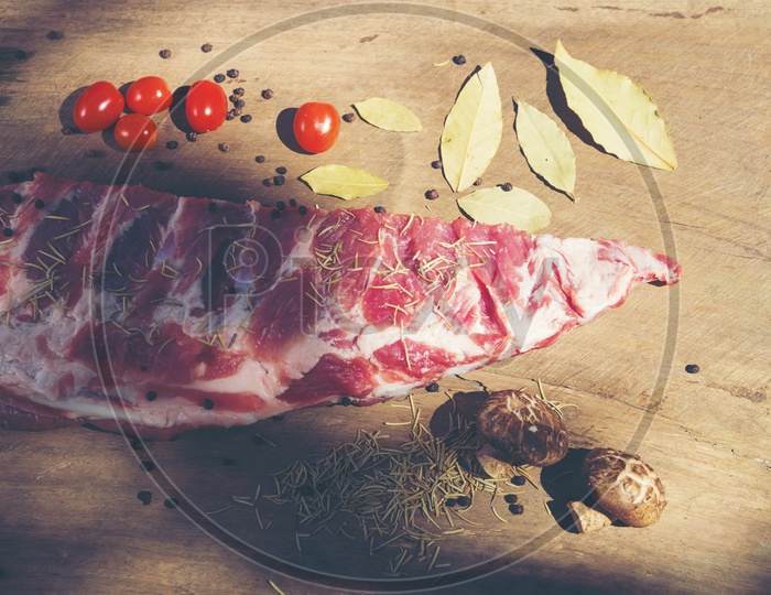 Fresh piece of pork ribs, Tomatoes, red chillis, pepper and herbs on a wooden cutting board