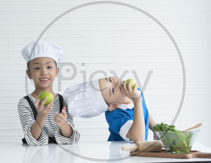 A boy and a girl are playing with green apples as little chefs -  cooking concept
