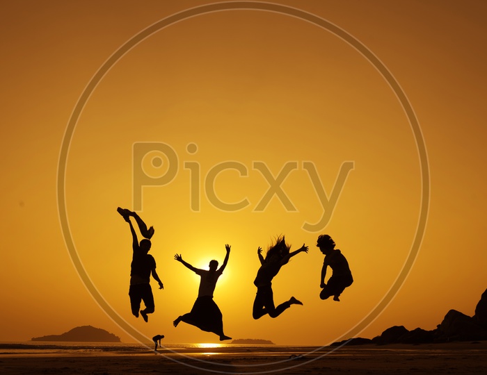 Silhouette Of People Happily jumping Over a Golden Sky In Background
