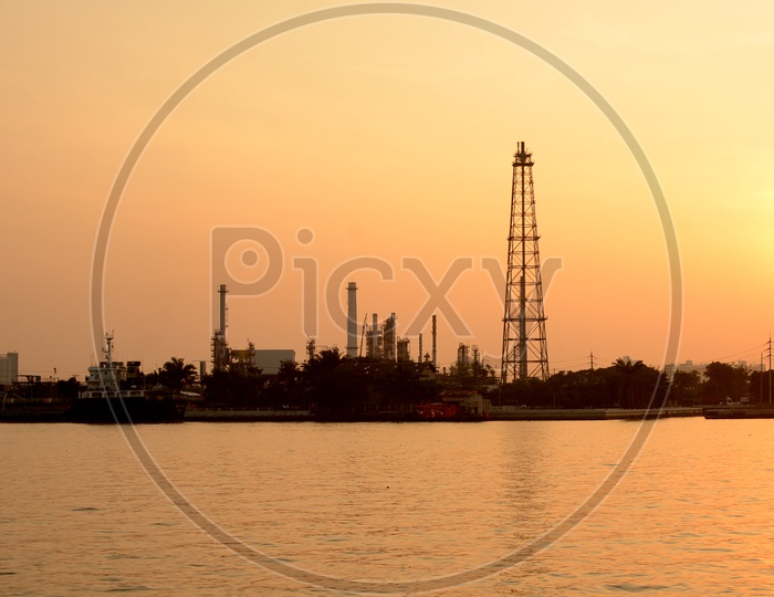 Silhouette of Oil Refinery Plat Besides Lake  With Exhaust Pipes And Towers of Industry over a Sunset Sky in Background