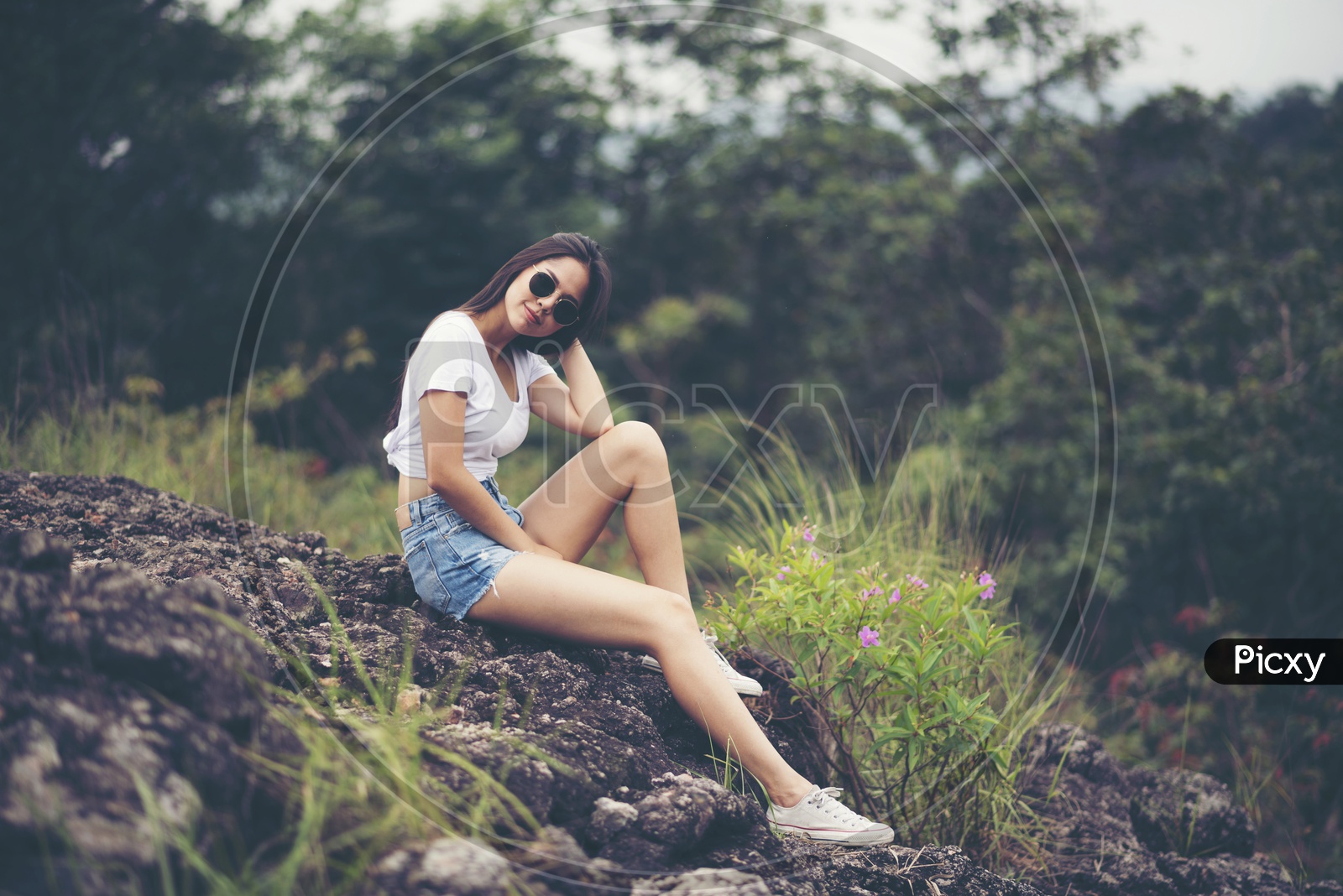 Asian Girl In Modern Wear Posing by Sitting on a rock in outdoor Background