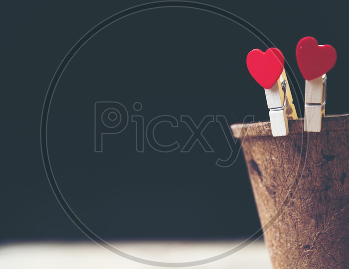 Heart shaped wooden clips holding a wooden cup with black background