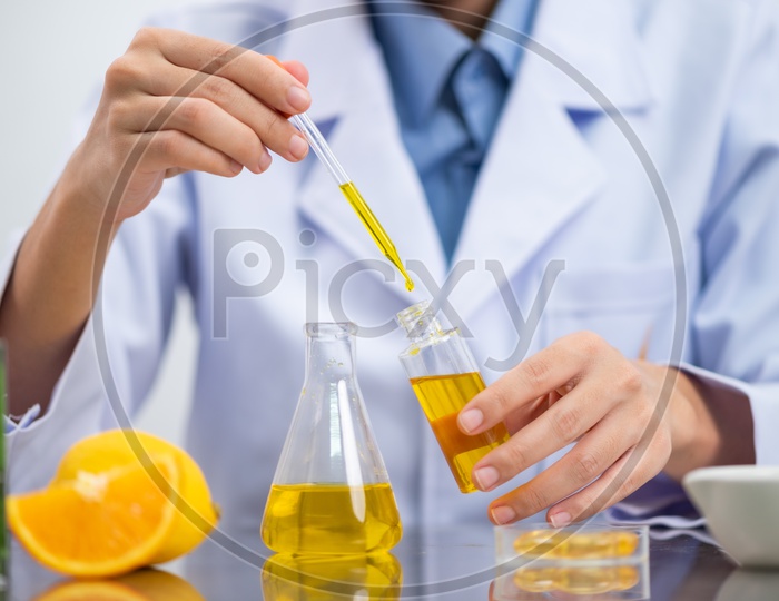 Asian Research Scientist in Laboratory Testing Bio Fuel Solutions in Test Tube with Orange Slices