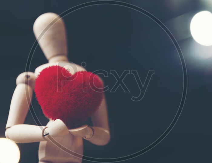 Close up of a wooden human shaped toy holding a soft fur heart shaped toy with black background