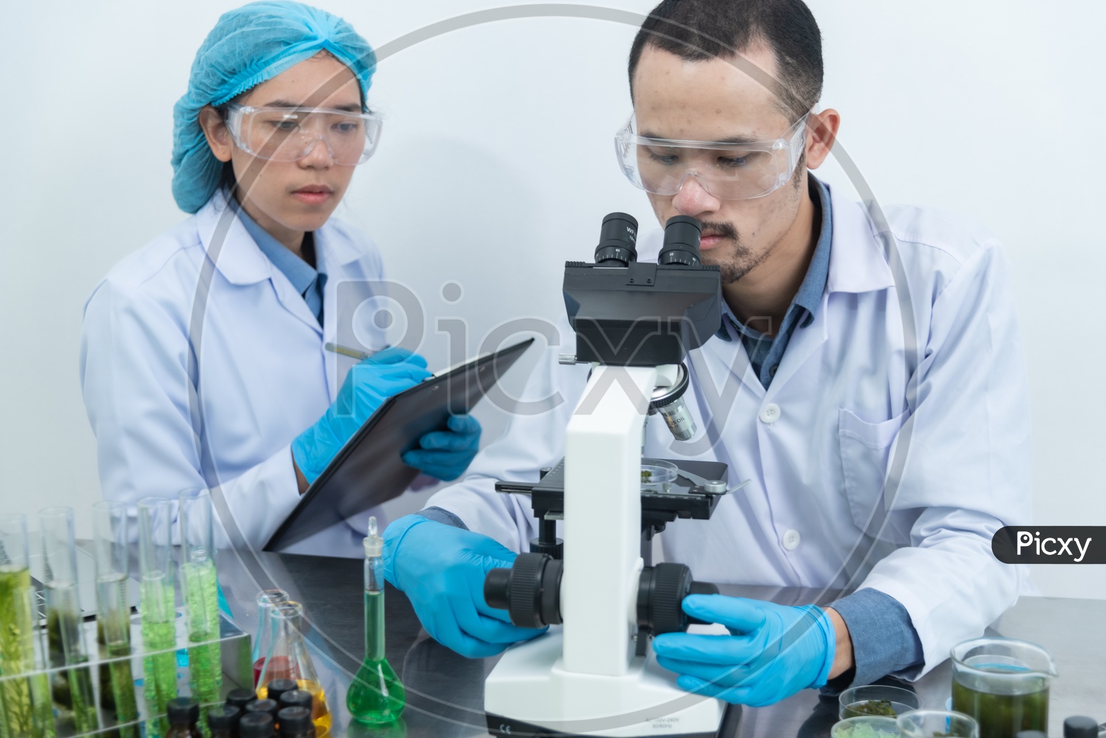 Asian Scientists using the Microscope for Researching Natural Extracts in Modern Laboratory