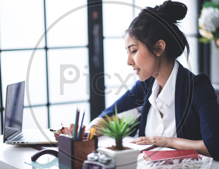Portrait of Pretty Young Asian Businesswoman using Mobile or Smartphone at Workplace
