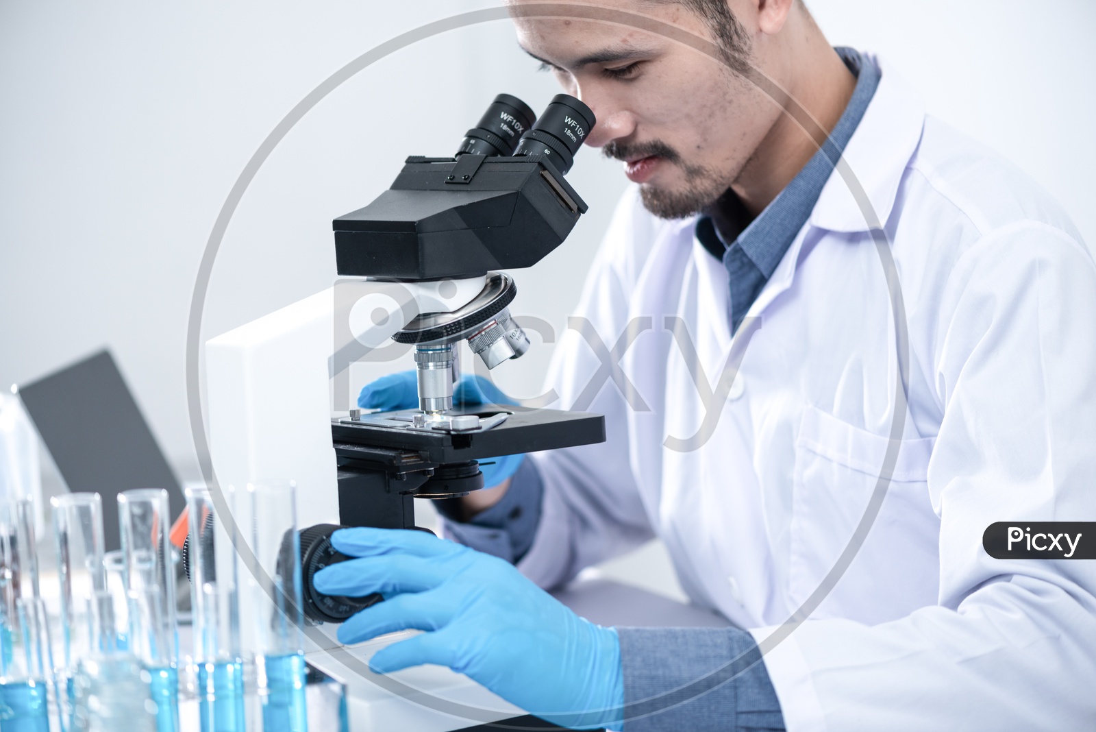 Asian Male Scientist or Medical Student Analyzing Sample through Microscope