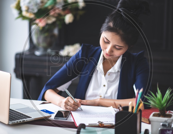 Portrait of pretty young businesswoman writing on Notes while working on Laptop at Workplace