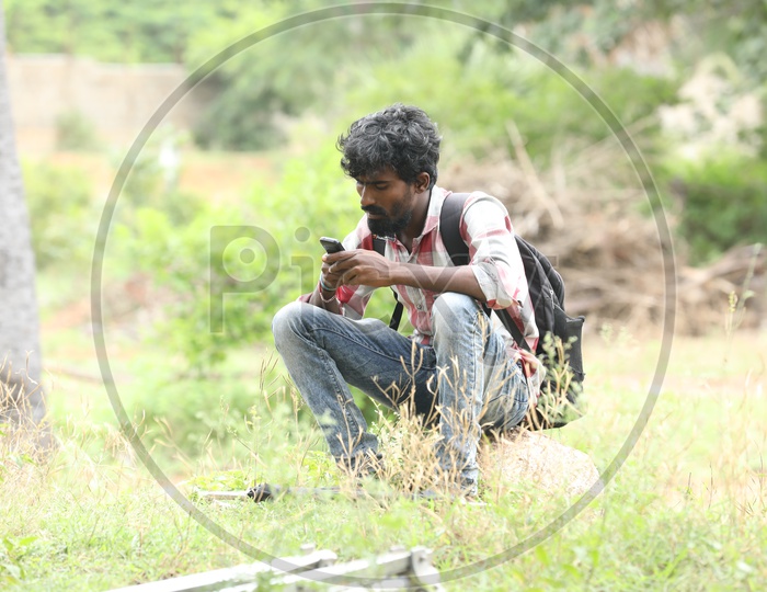 Indian Bearded boy sitting with a backpack using mobile phone