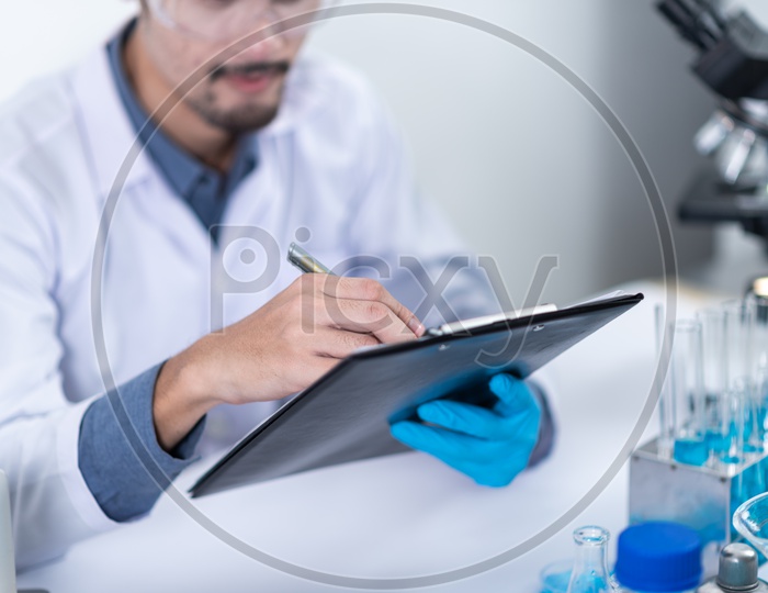 Asian Male Scientist Writing down Test Results on Paper at Laboratory