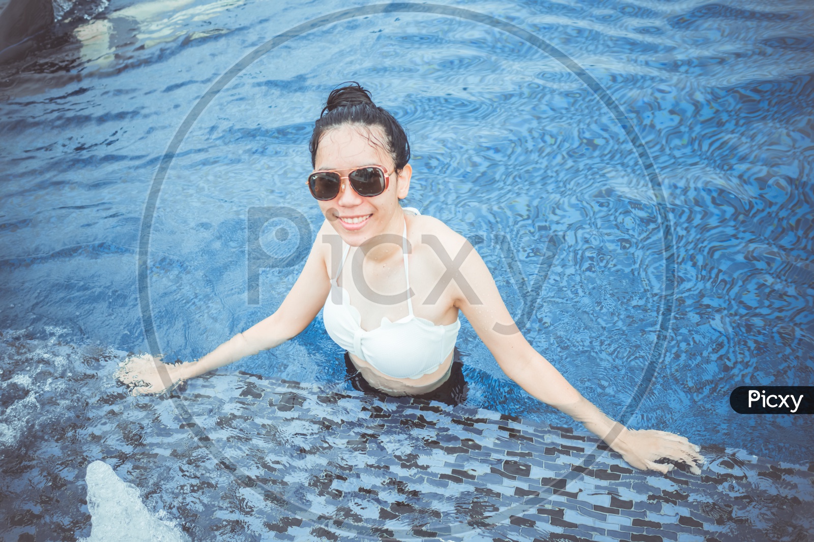 Asian Woman wearing sunglasses posing by the swimming pool