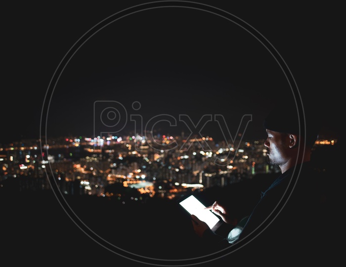 A Man using tablet over the mountain city view at night